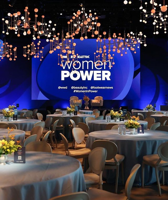 A corporate stage under blue lighting with suspended installations above banquet tables