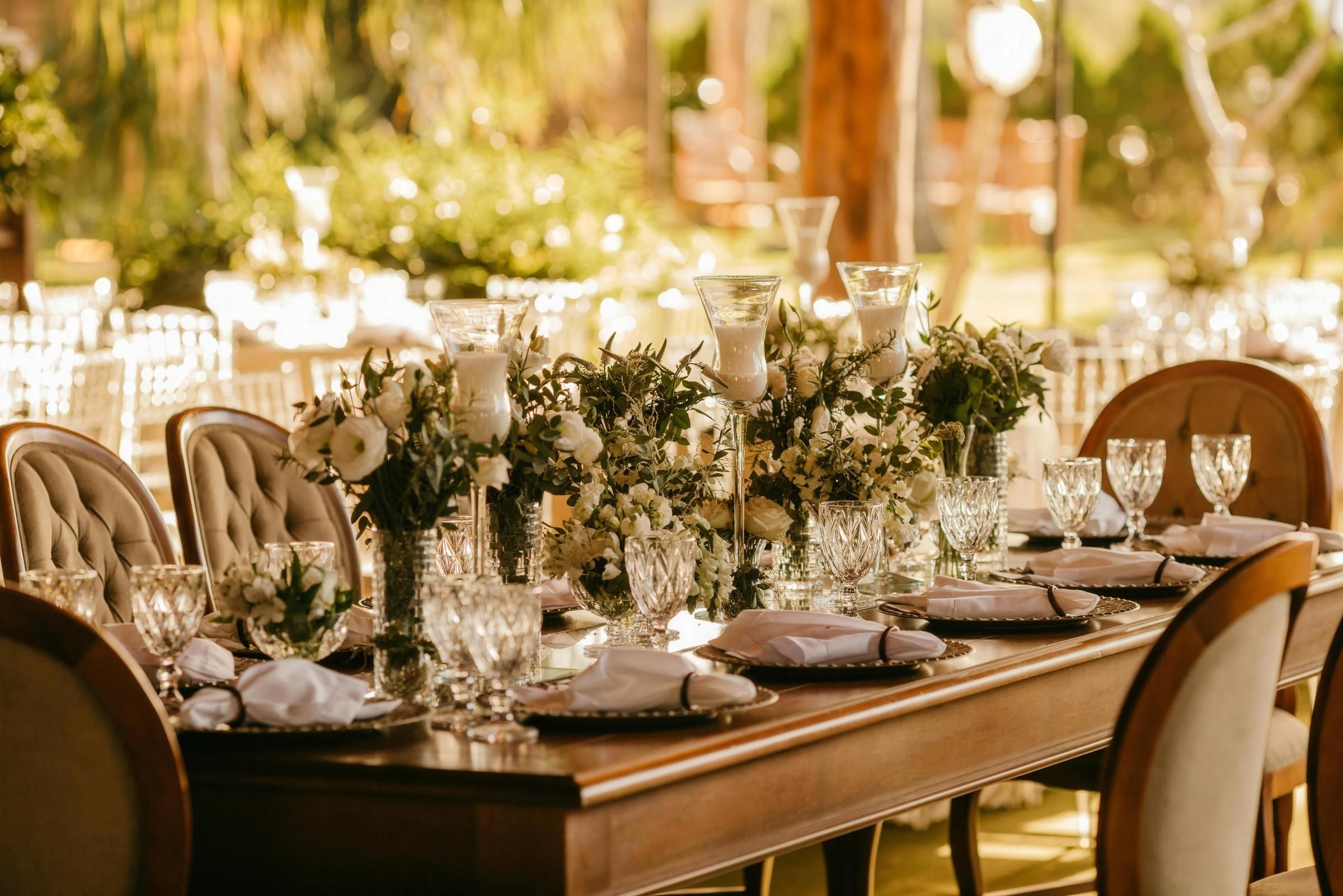 A long banquet table dressed with white florals, crystal glassware and candlelight at a Curated Luxe garden reception