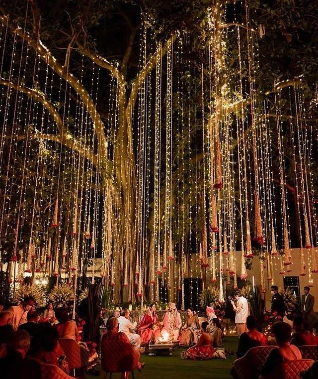 An outdoor wedding ceremony beneath trees curtained in cascading fairy lights